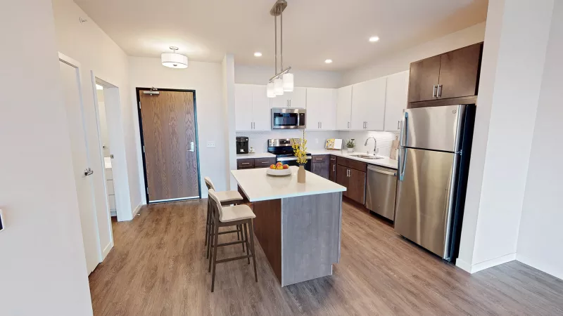 Modern kitchen with an island, white and dark wood cabinets, stainless steel appliances, and wood-look flooring.