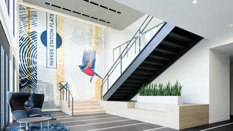 Modern lobby with a colorful mural featuring a bird and abstract designs, a dark industrial staircase, and blue armchairs.