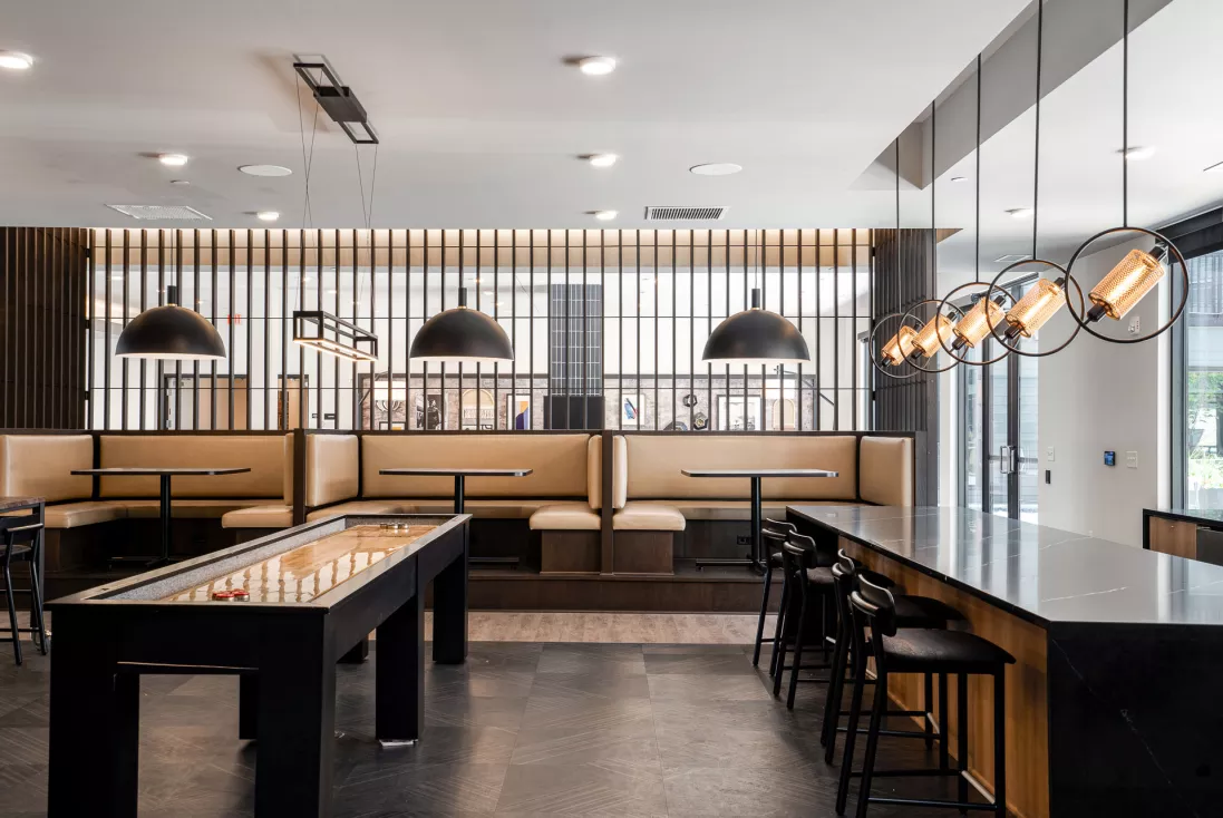 Modern recreational room with shuffleboard, dark counter with stools, and light brown booths under stylish pendant lights.